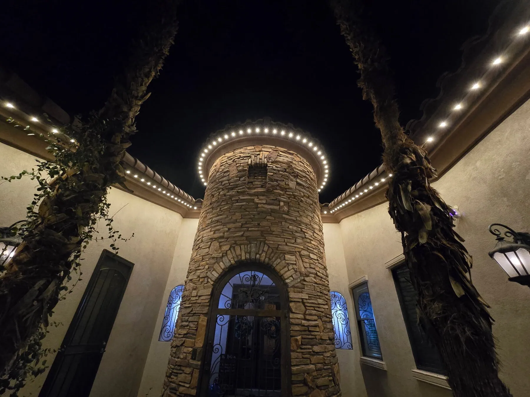 White permanent lights around a stone entry tower and courtyard roofline