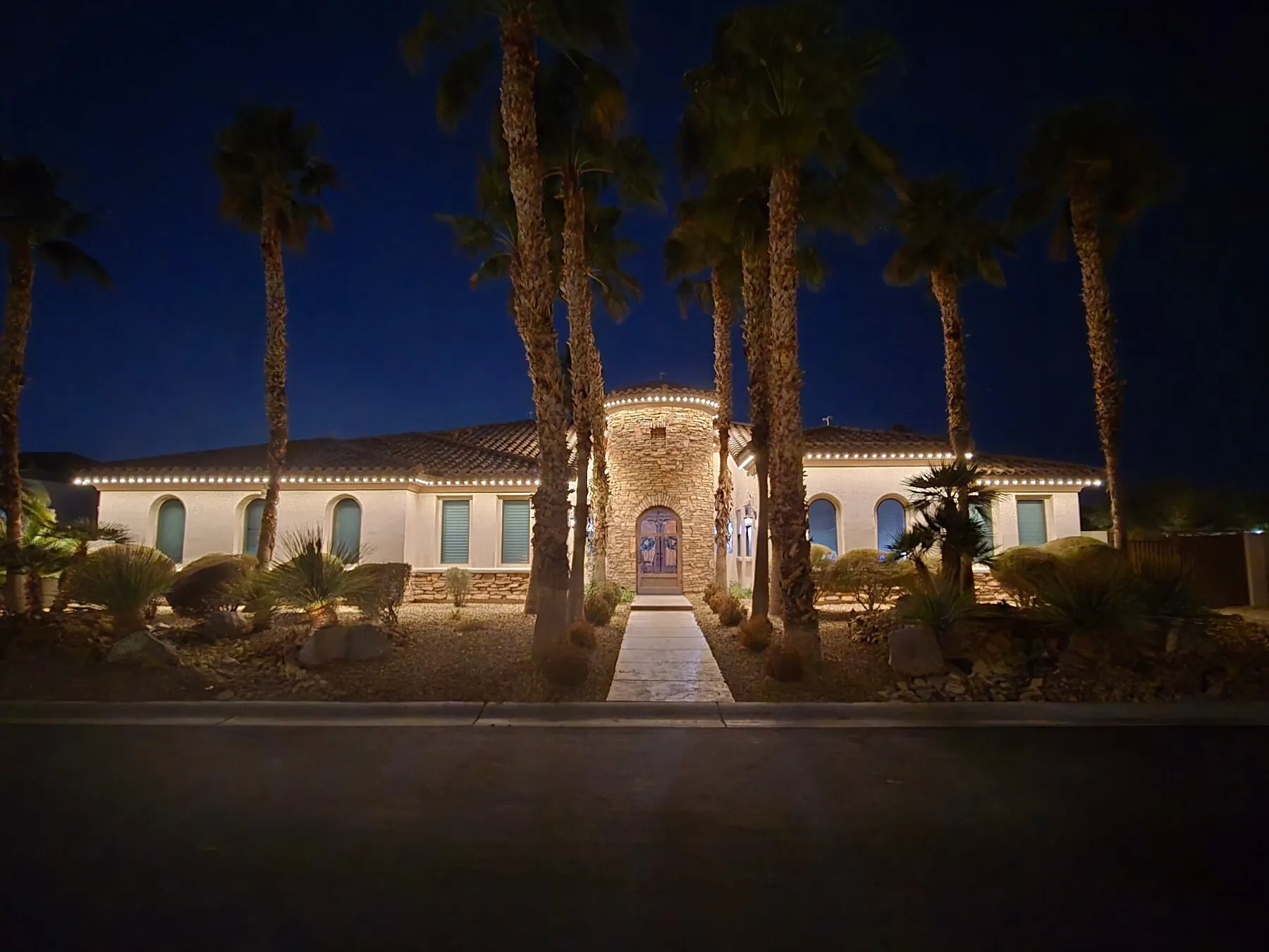 Warm white roofline lighting on a home framed by palm trees