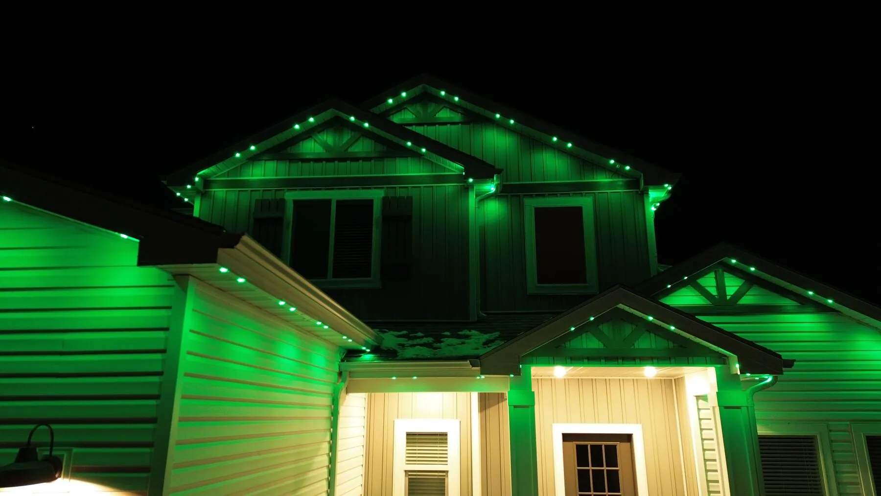 Green permanent lighting across the front of a two-story home