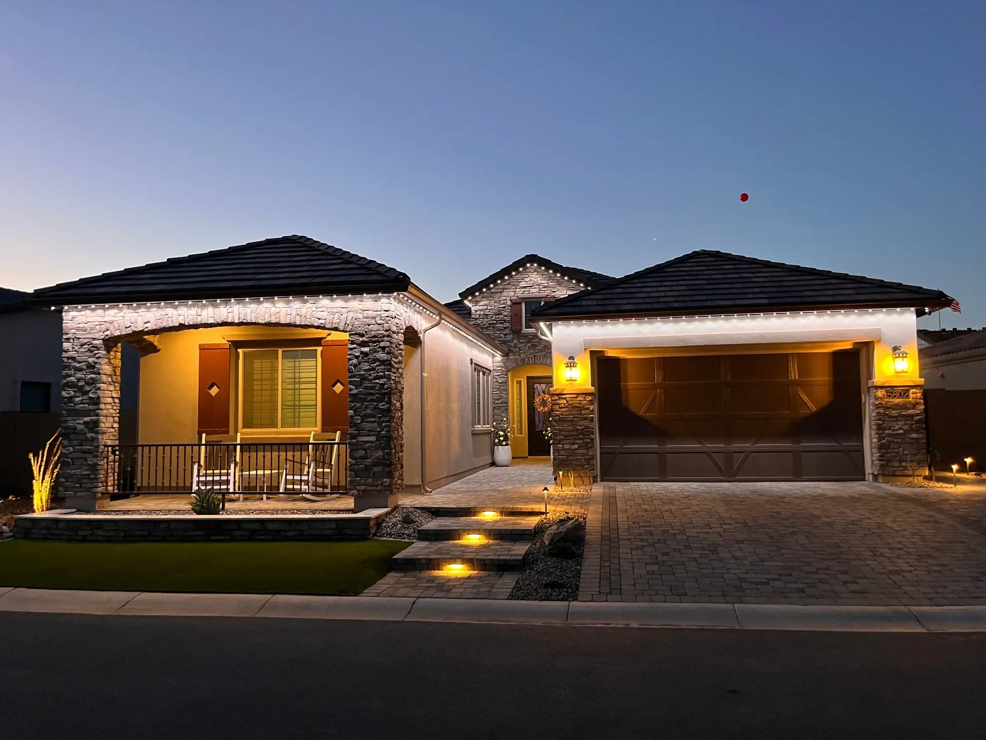 Warm-white roofline lights outlining a stone-front home at dusk