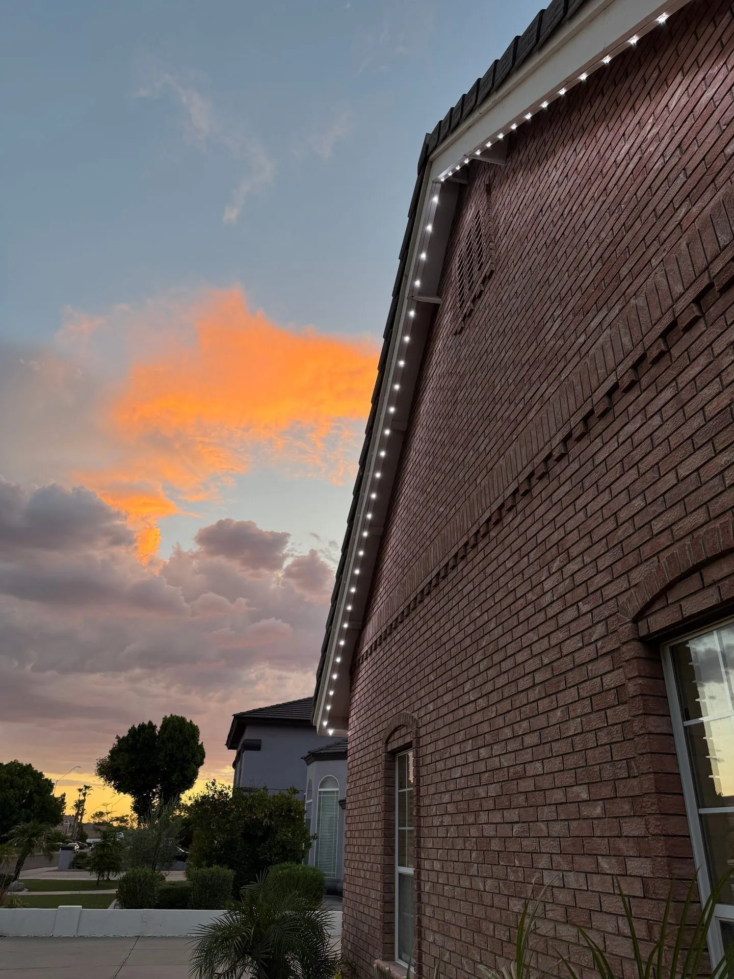 White roofline lights along a tall brick exterior beneath a sunset sky