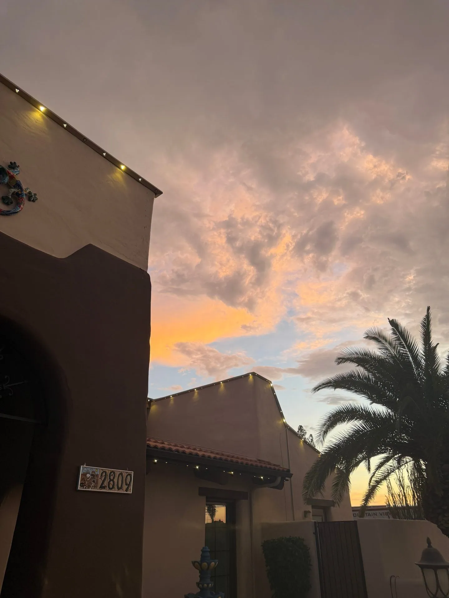 Soft white roofline lights on stucco homes beneath a colorful sunset sky