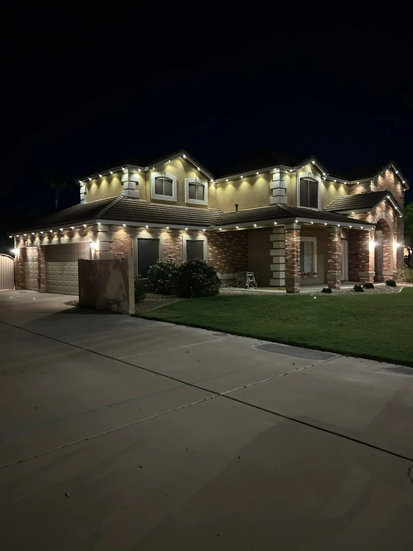 Warm white roofline lights on a two-story brick home at night