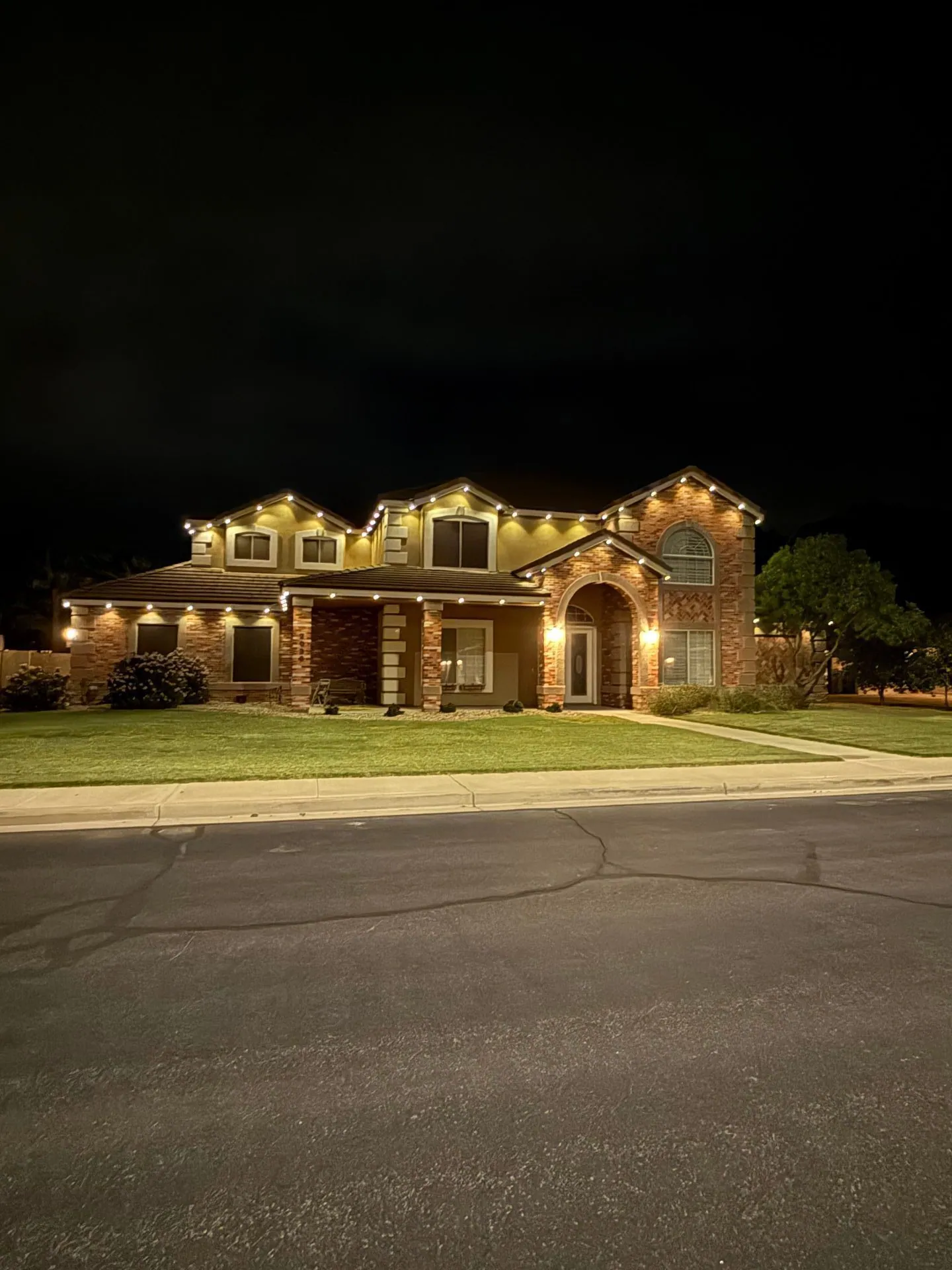 Warm roofline and facade lights on a large two-story brick home at night