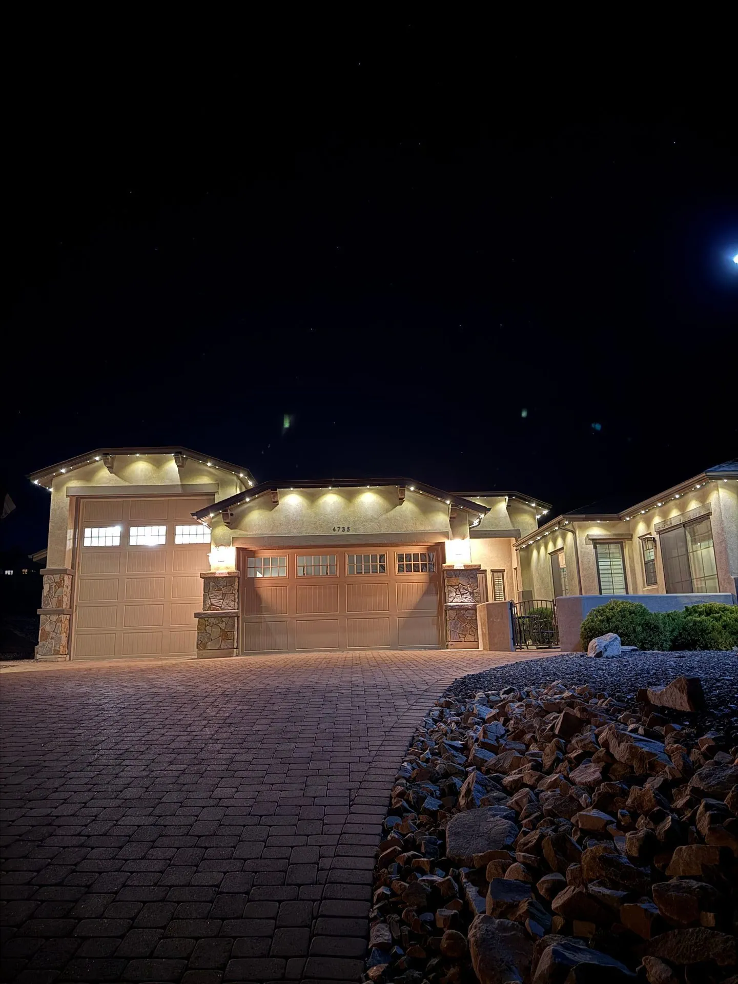 Warm permanent lighting on custom home with pavers