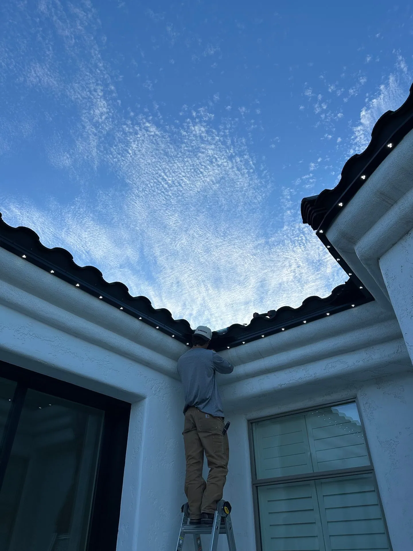 Technician installing permanent lighting on home roofline