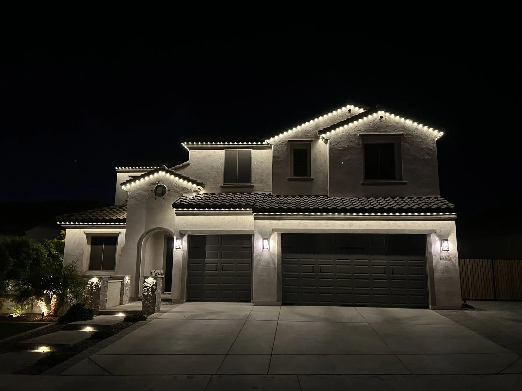Warm white lighting along a two-story home's roofline and garage