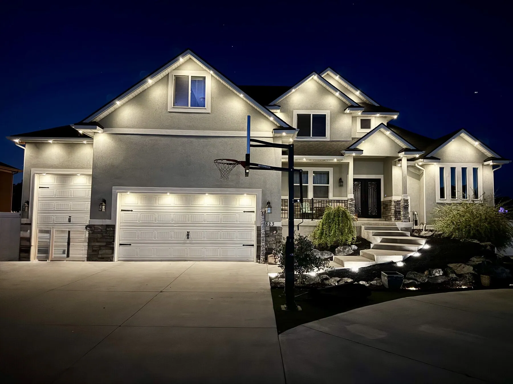 Warm white roofline lighting on a two-story home with landscaping