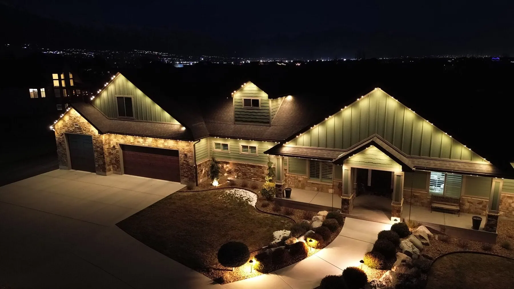 Aerial view of warm white roofline lighting on a stone and siding home